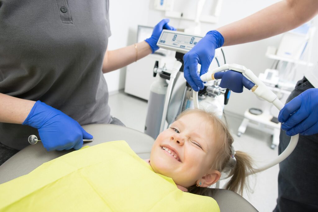 pexels photo 8260438 8260438 A cheerful child winks while sitting in a dental chair, surrounded by dental professionals.